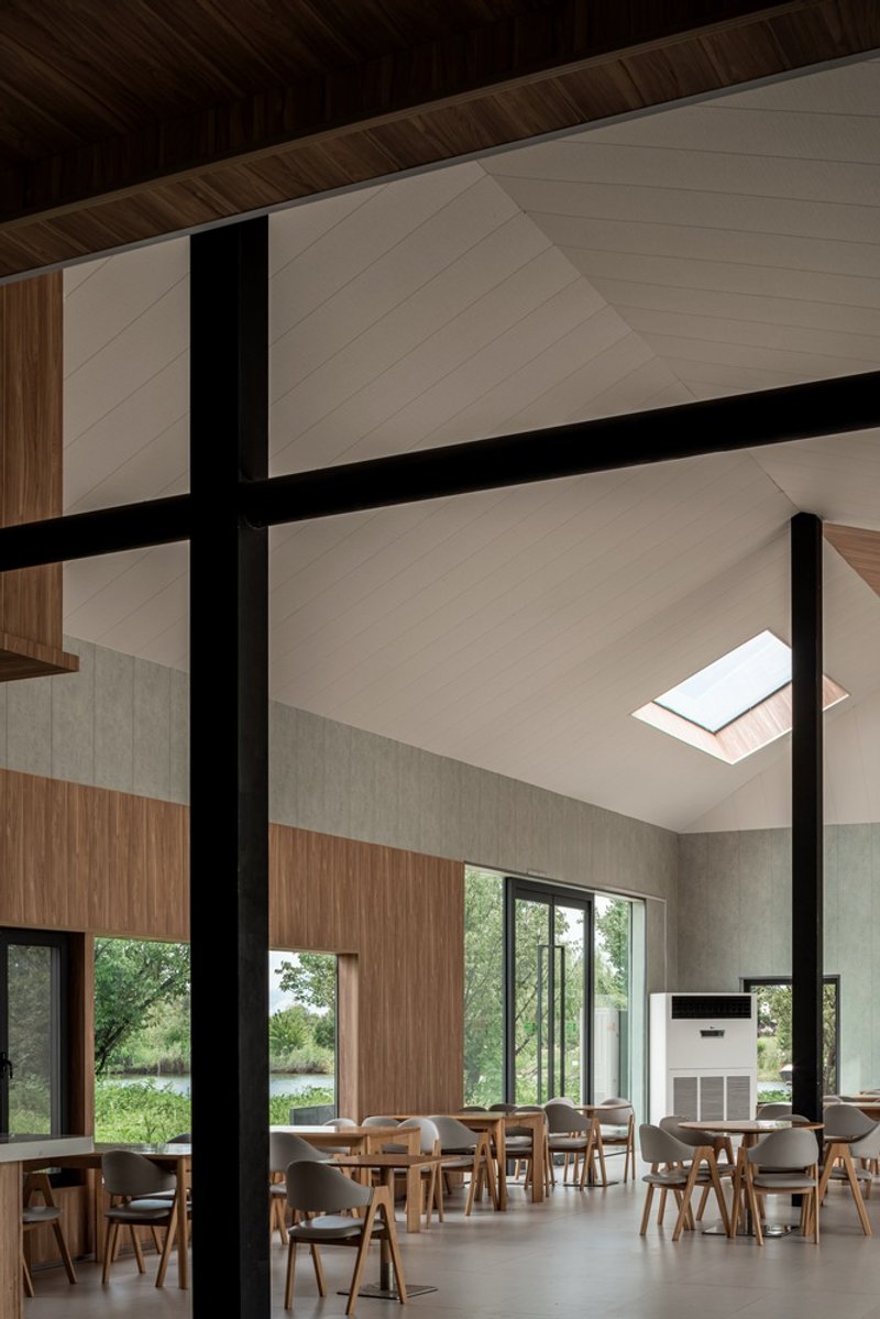 Double-height dining hall with exposed black steel columns and skylights above timber-clad walls