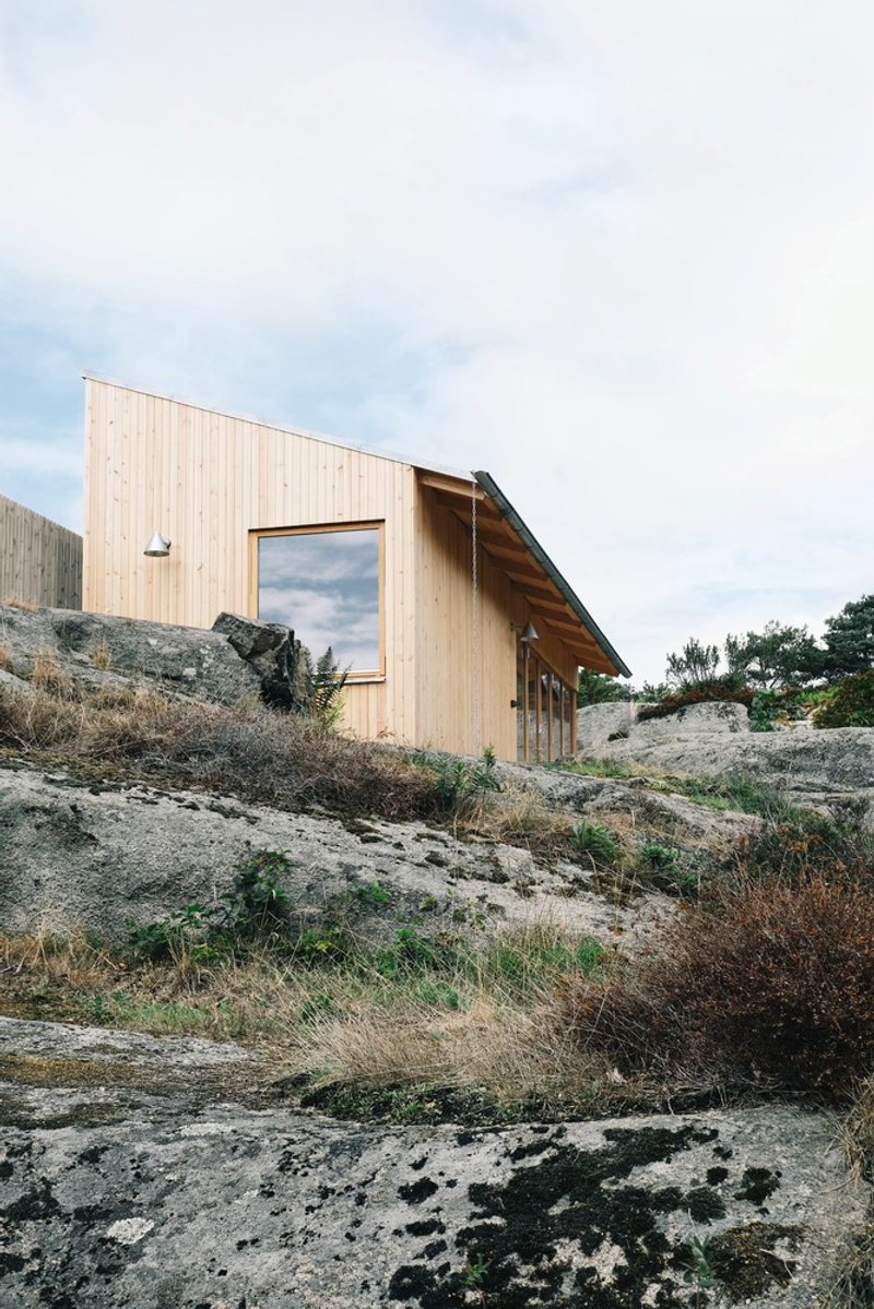 Vertical timber cladding and sloped metal roof nestled into rocky outcrop with scattered vegetation