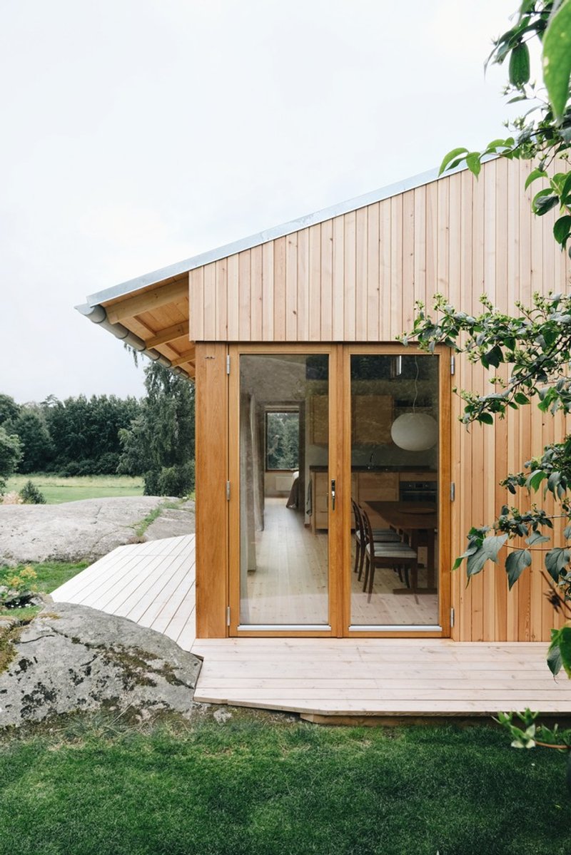 Vertical timber cladding with glazed double doors opening onto a timber deck beside vegetation