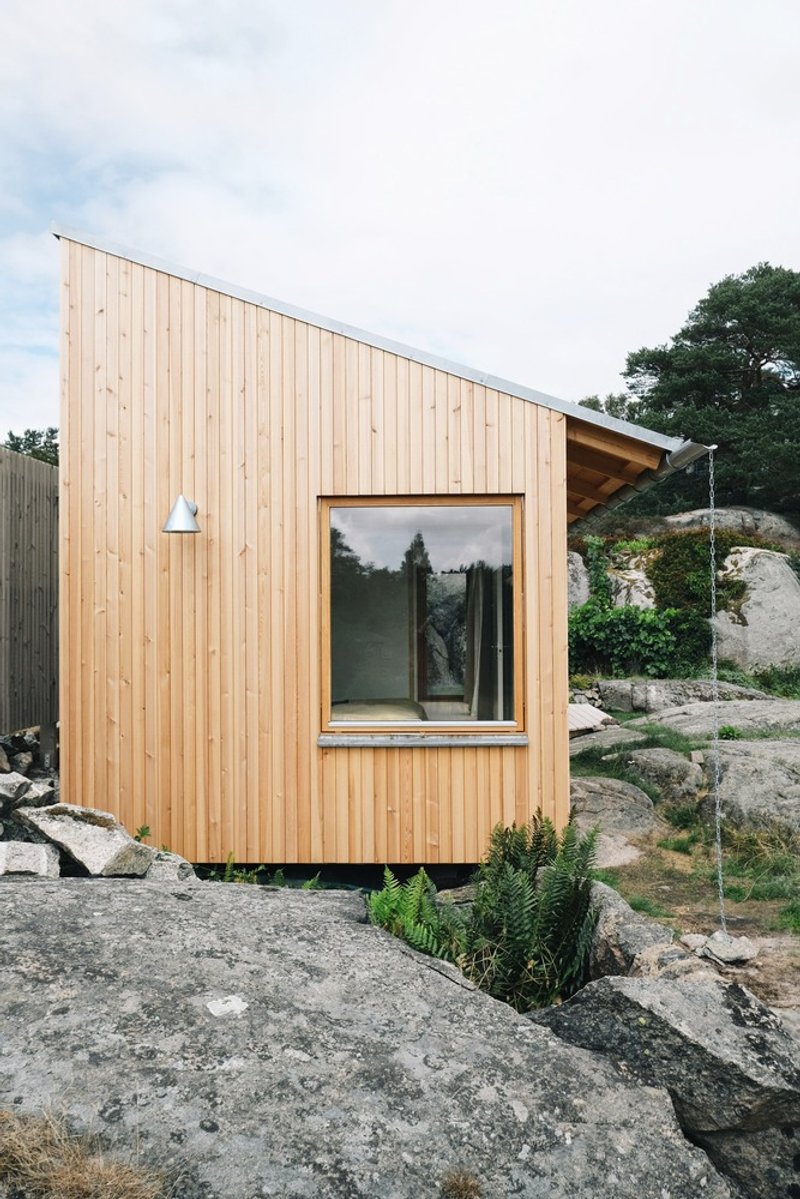 Timber-clad end wall with square window and exterior light fixture on exposed rock terrain