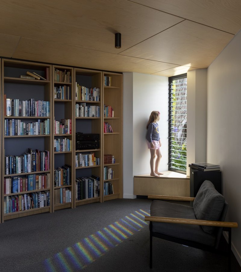 Library with timber shelving and window seat where a child stands silhouetted against louvered glass