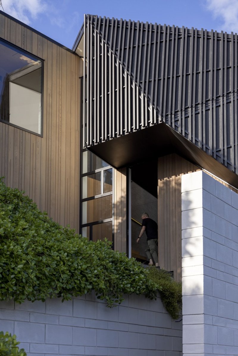 Cantilevered upper volume with vertical metal screening above timber-clad bridge and white tiled base