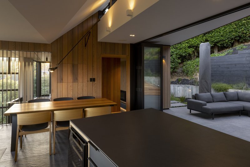 Open plan kitchen and dining space with timber walls opening onto a landscaped courtyard terrace