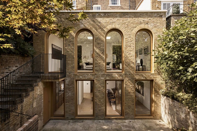 Rear facade of brick townhouse extension with arched windows and glazed doors opening to courtyard in dappled sunlight