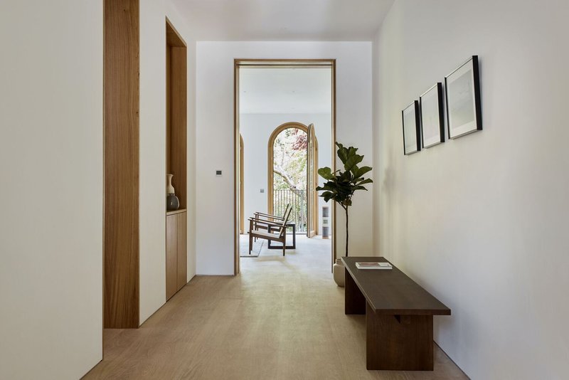 Interior hallway with timber doors and arched window at end opening to terrace with chair and potted plant