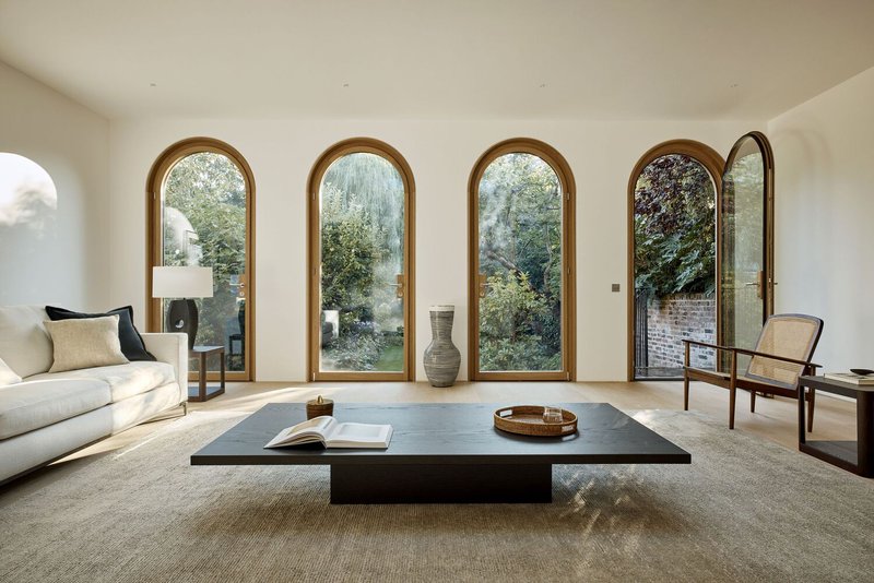 Living room with row of arched windows framing garden views through timber frames and deep reveals