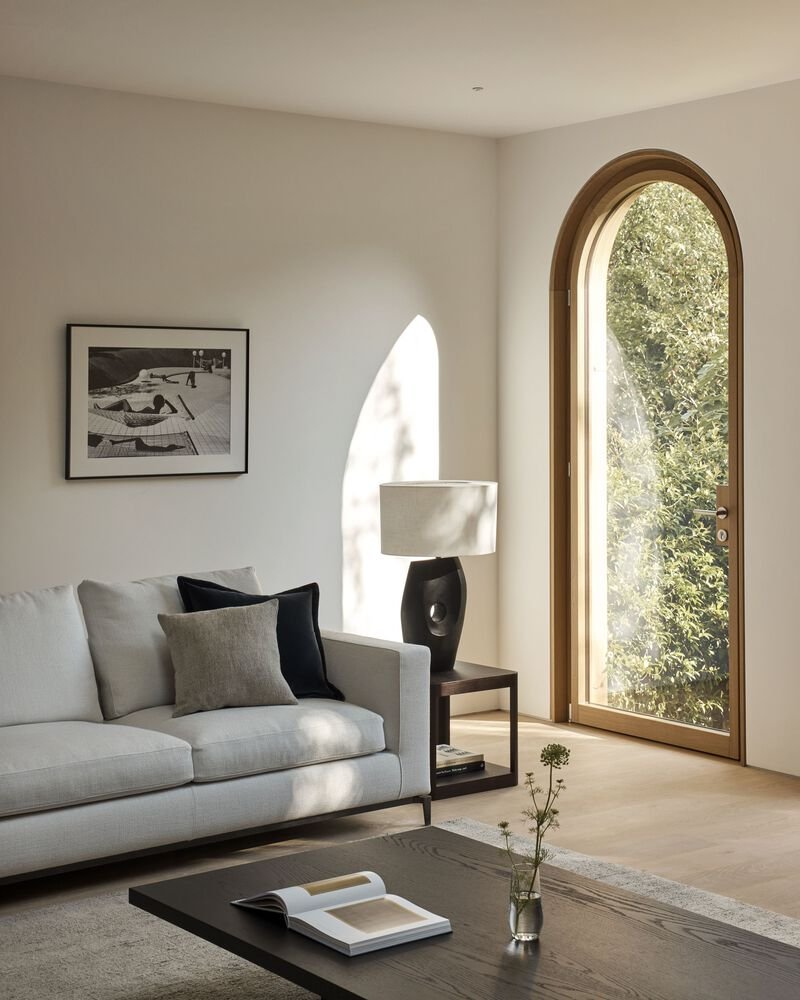 Tall arched window with timber frame casting sharp afternoon shadows across pale plaster walls