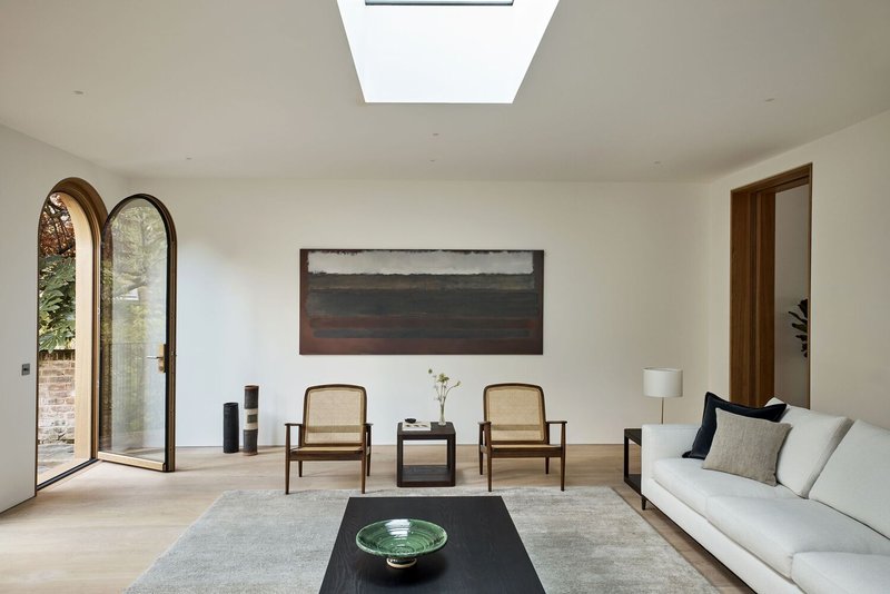 White-walled living room with rectangular skylight and arched door framing garden view in autumn