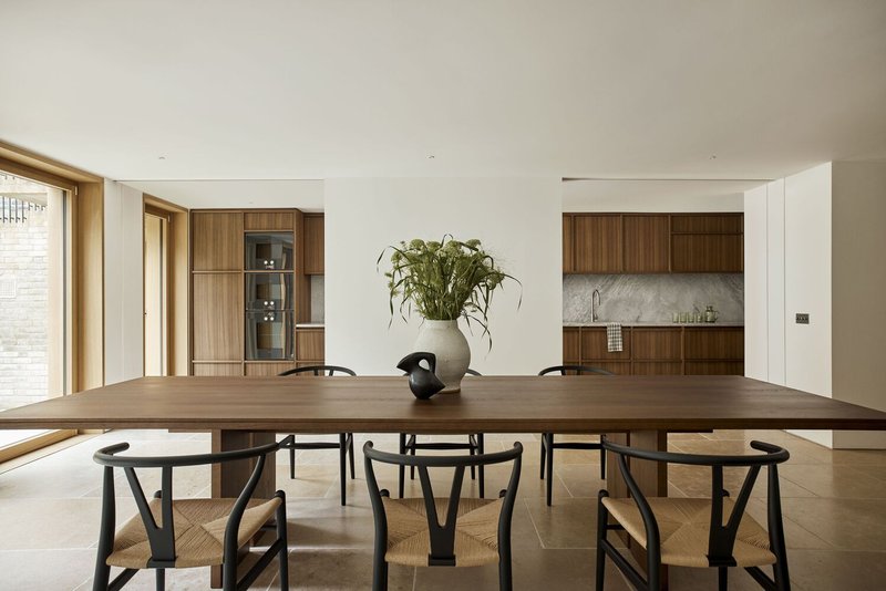Open-plan dining and kitchen space with timber table, walnut cabinetry and stone tile flooring