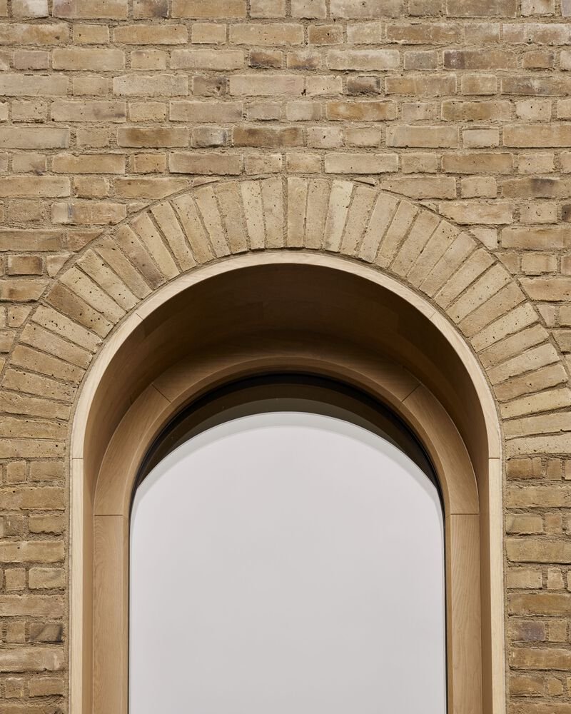 Close-up of an arched window opening showing brick voussoirs and recessed timber frame