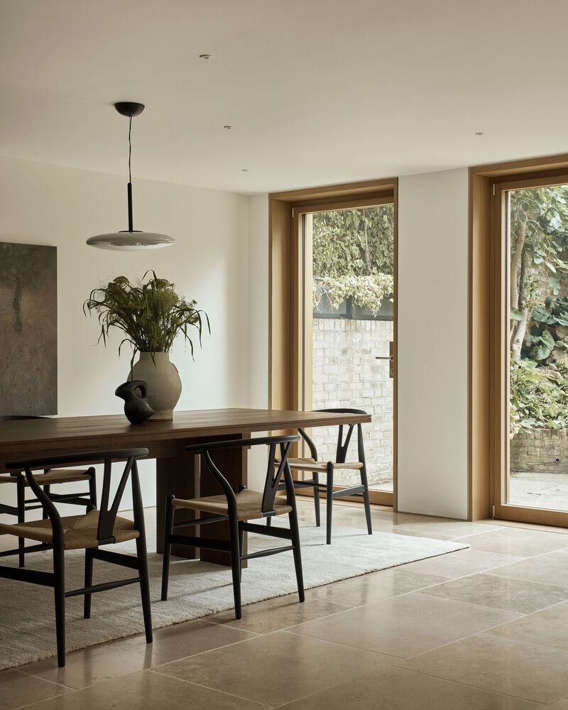 Dining area with timber table, wishbone chairs and full-height windows framing garden views
