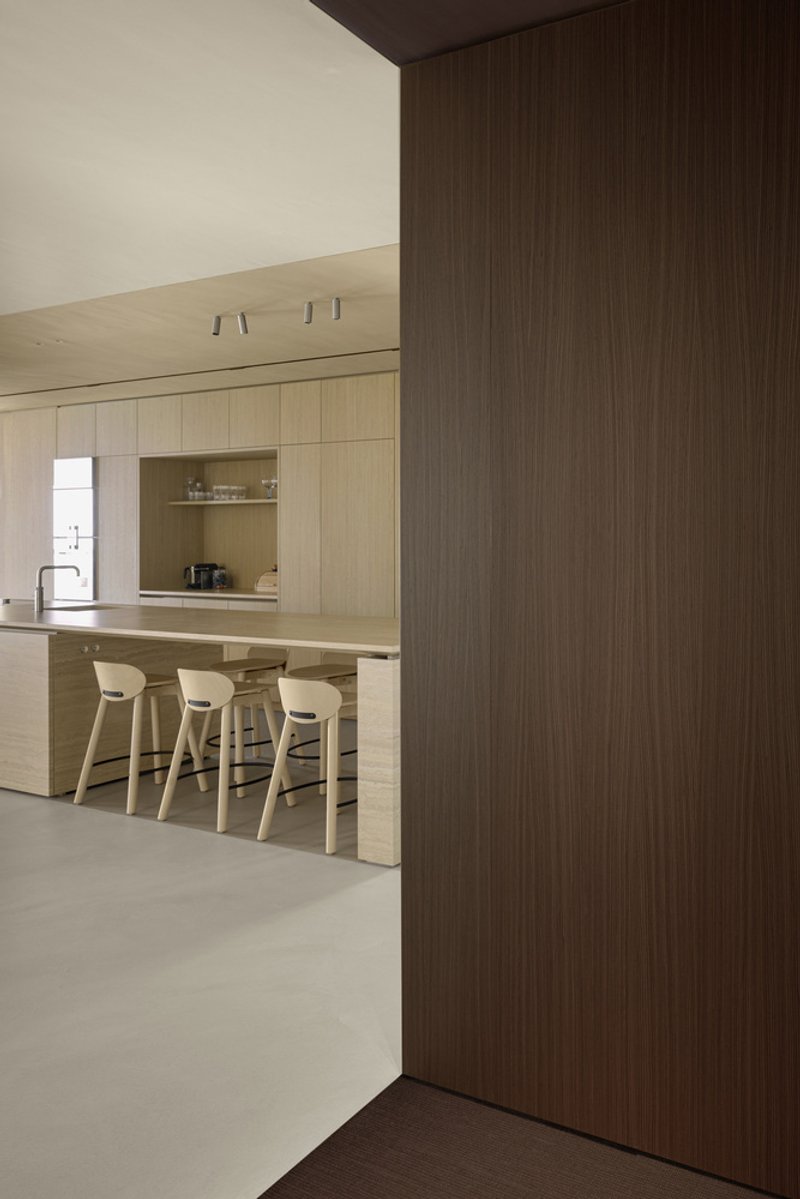 View through dark timber doorway revealing kitchen island with bar stools in distance