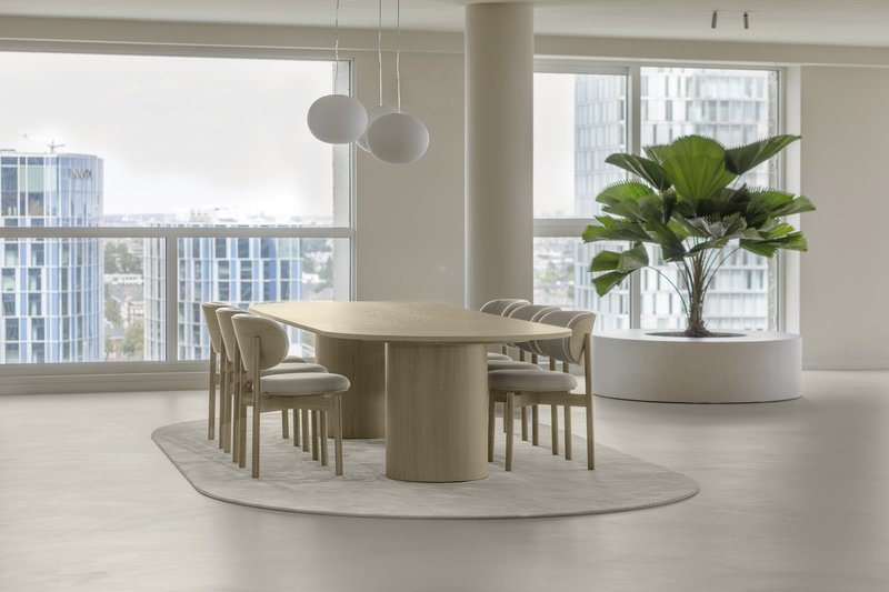 Cylindrical pedestal dining table on an oval rug with floor-to-ceiling windows overlooking the cityscape