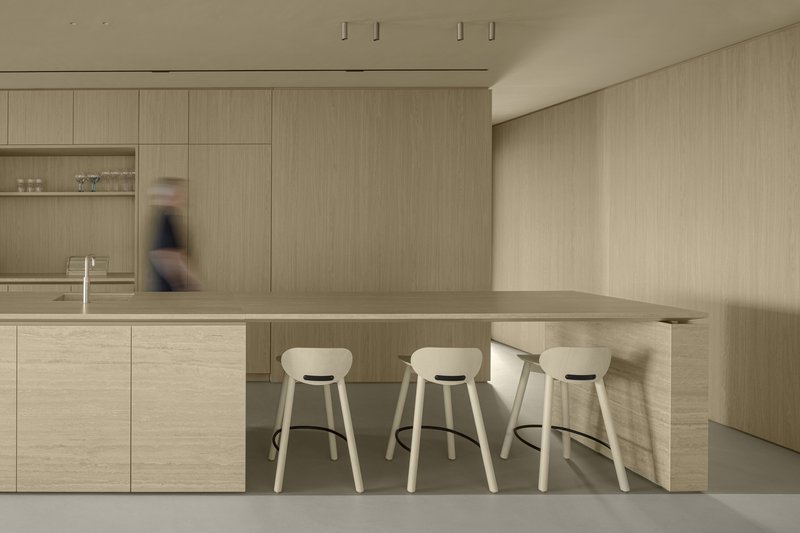 Kitchen island with three pale stools and a figure passing behind in soft light