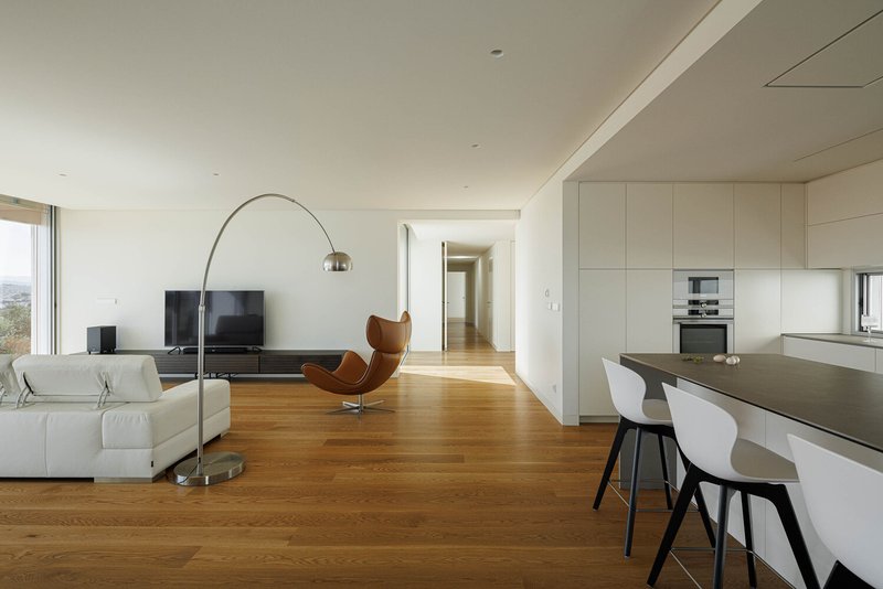 Open-plan living space with oak flooring linking white kitchen island to lounge area in daylight