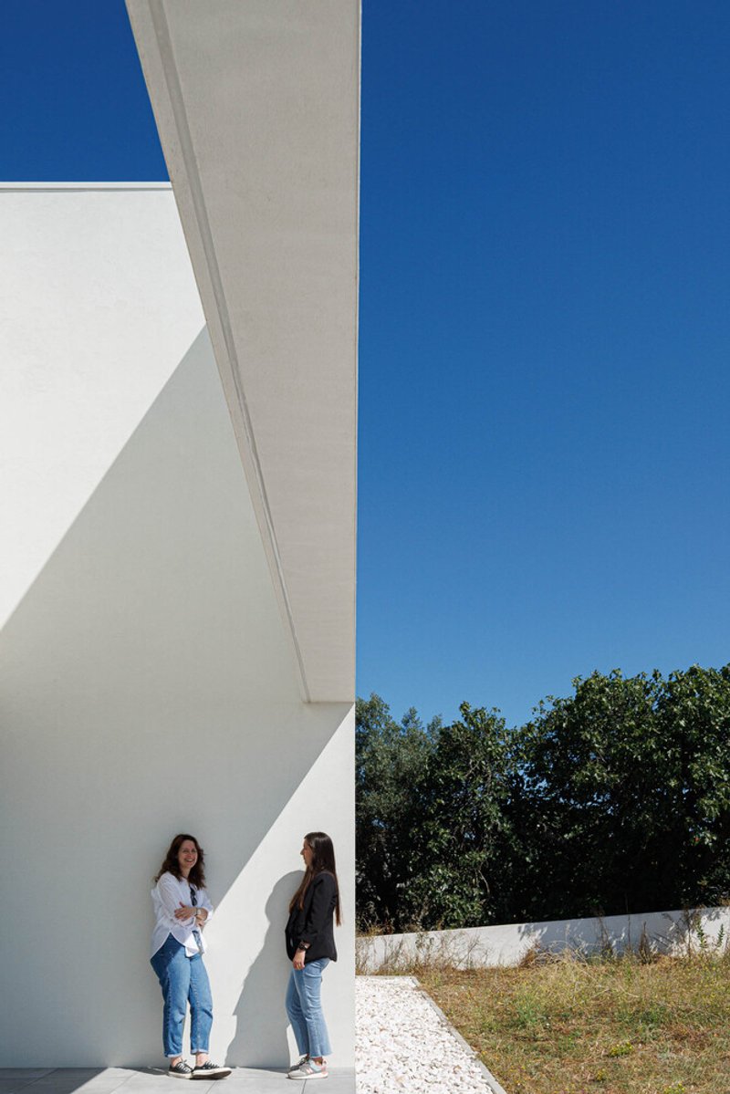 Two figures standing beneath a cantilevered white overhang with geometric shadows on a sunny day