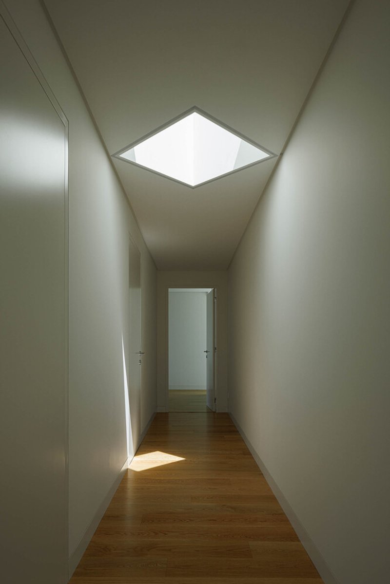 Narrow corridor with oak flooring and square ceiling skylight illuminating white walls