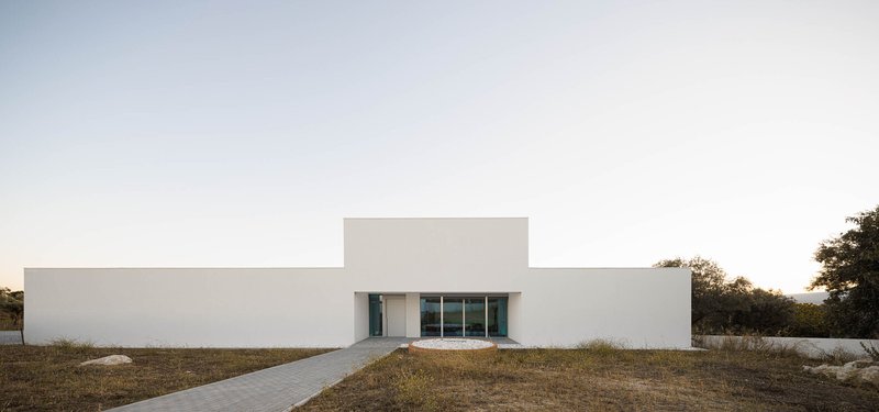 White stucco facade with stepped massing and glazed entry set in dry grassland