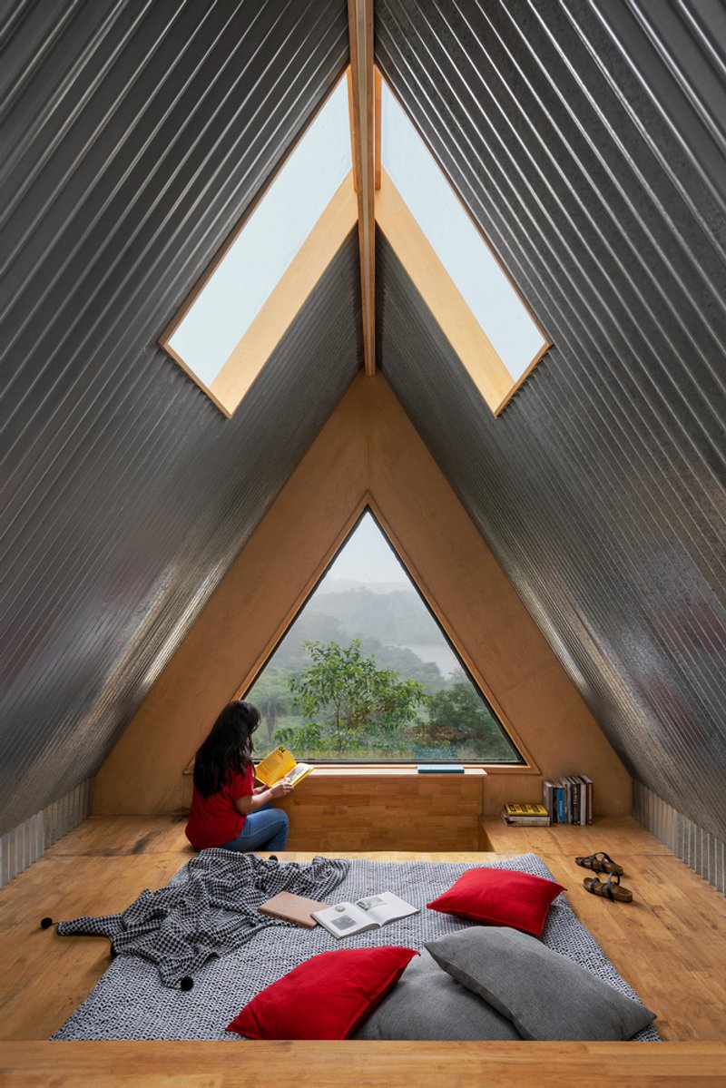 Interior view of the triangular window seat with corrugated metal roof planes and a person reading