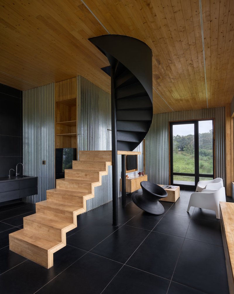Black spiral staircase and timber steps beneath a tongue-and-groove plank ceiling with corrugated metal walls