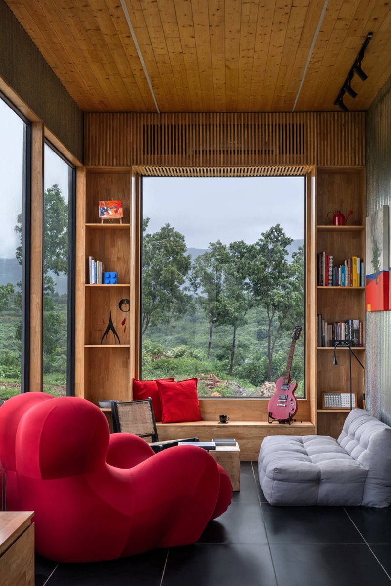 Timber-lined window seat with built-in shelving flanked by full-height glazing overlooking green hillside