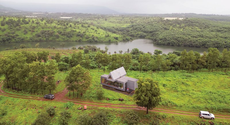 Aerial view of the A-frame structure surrounded by trees and green fields near a river bend