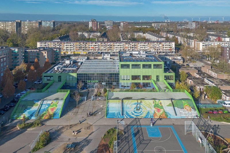 Aerial view of the green school building with rooftop solar panels and painted sport courts below