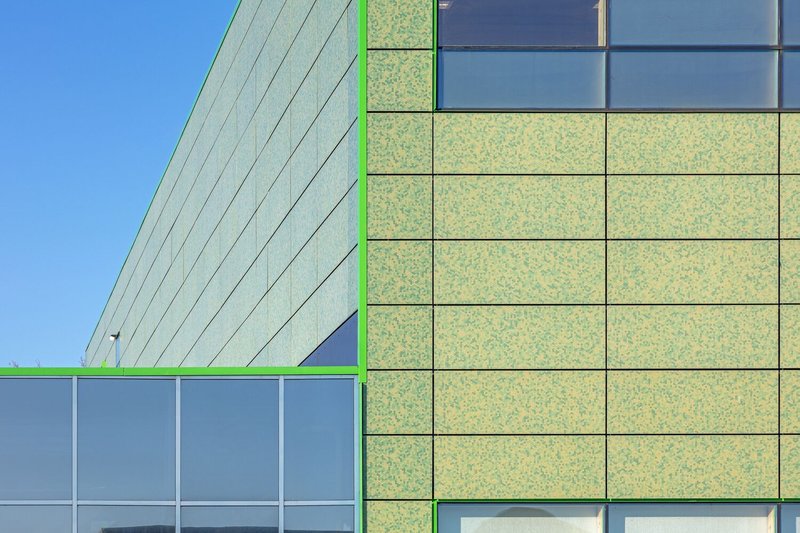 Corner detail of the facade showing green panel joints and window mullions against a clear sky