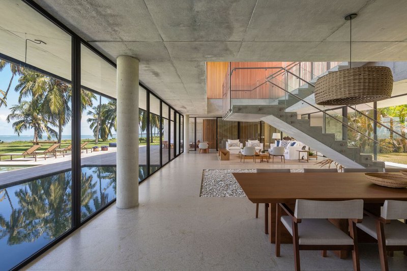 Ground-floor interior: dining table, concrete stair, pool reflection through full-width glazing