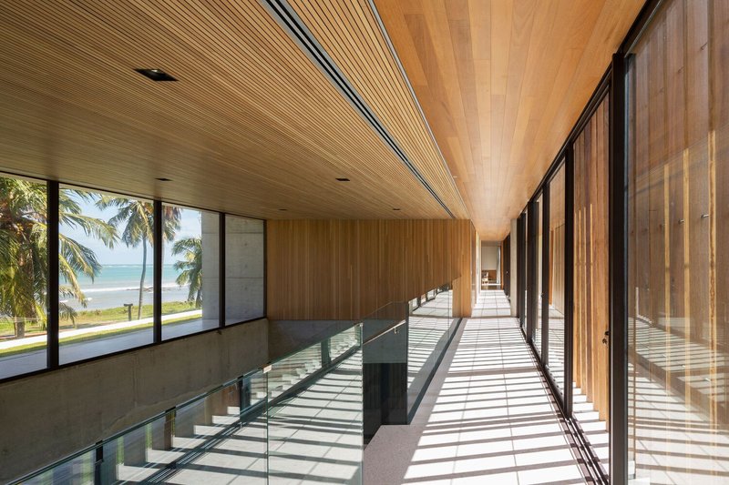 Upper-floor corridor: timber-lined ceiling, glass balustrade overlooking the double-height void, sea view