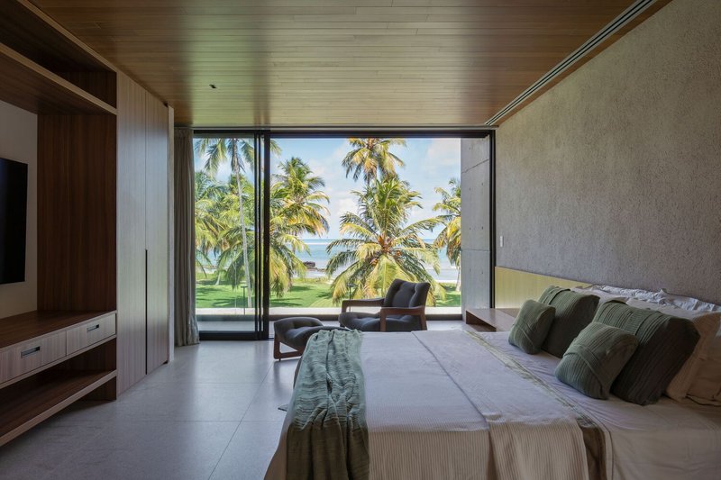 Master bedroom: timber ceiling, stone accent wall, full-width sliding door to balcony with palm and ocean view