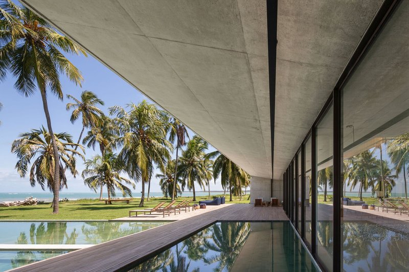 Covered pool terrace: concrete soffit, timber deck, infinity-edge pool reflecting palms and ocean