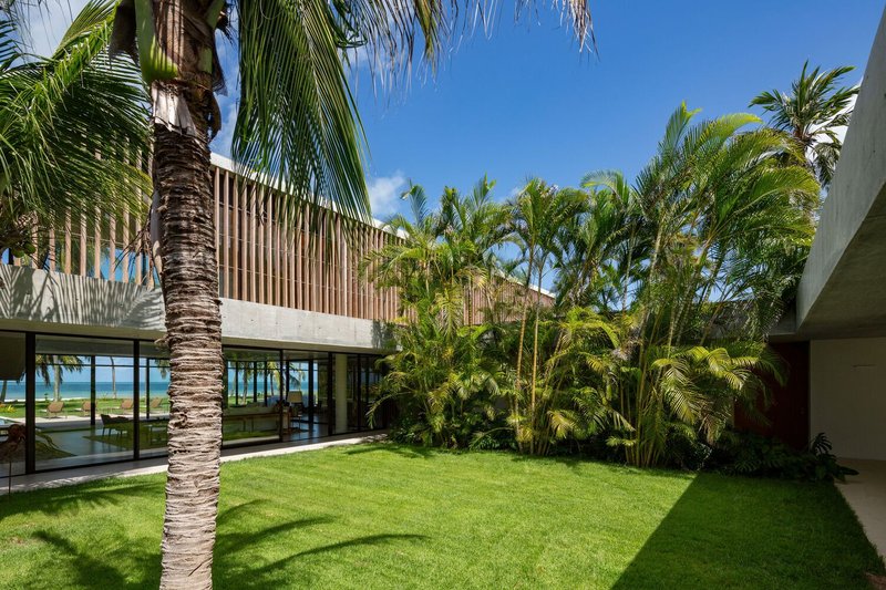 Internal garden courtyard: timber-screened upper volume, palm trees, glass walls, ocean visible beyond