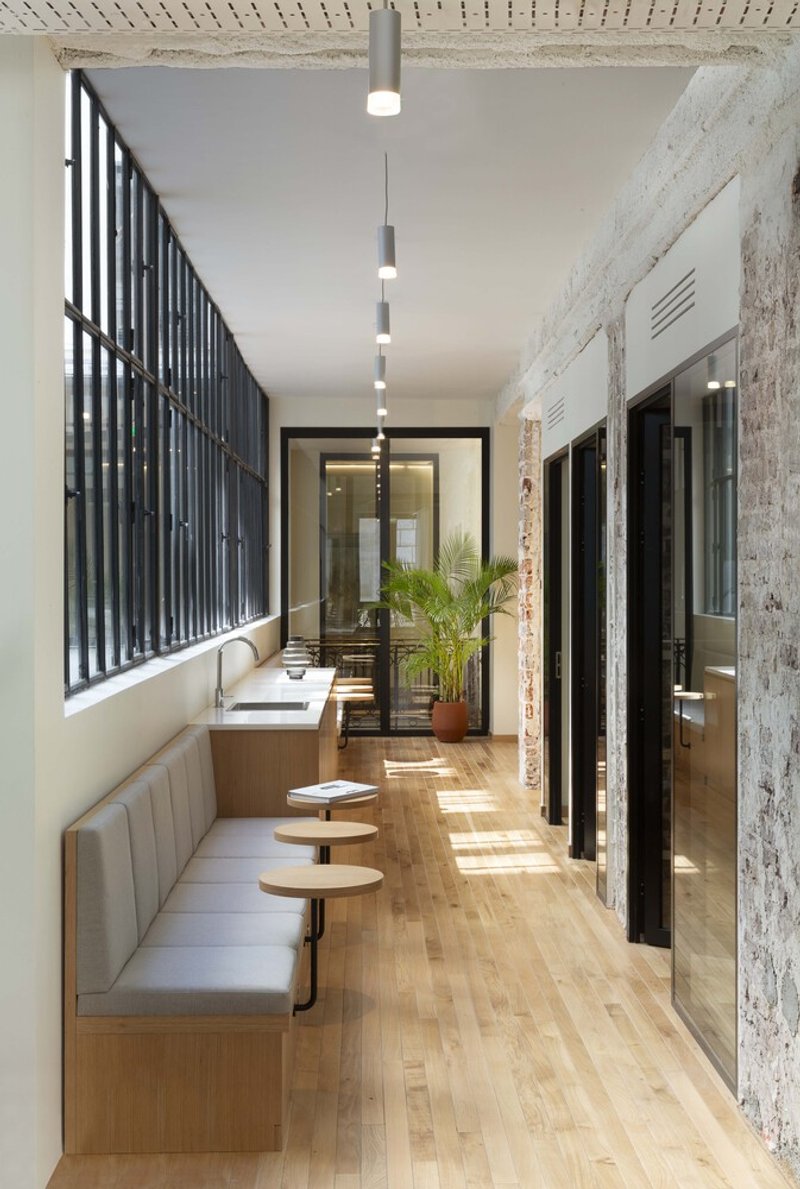 Narrow corridor with banquette seating: oak floor, steel-frame windows, pendant lights, pink cushions