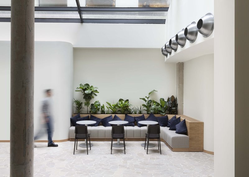 Courtyard lounge: glass roof overhead, concrete columns, built-in bench with plants, spherical chrome light fixtures