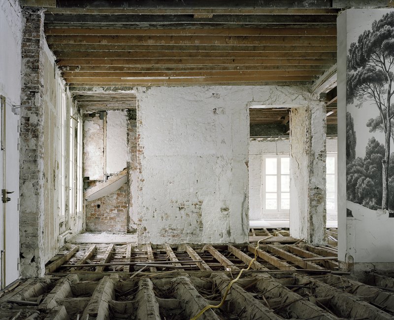 Before: stripped room with exposed timber joists, rubble, brick walls, faded mural wallpaper visible