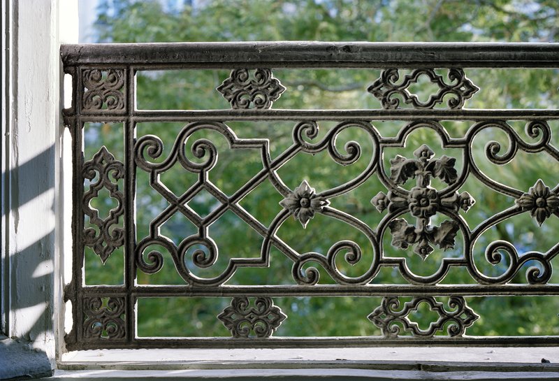 Before: ornate iron balcony railing detail, trees through the bars