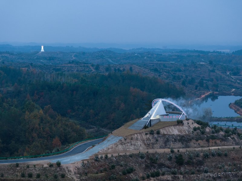 Dusk aerial: both interventions visible across the terraced hills, the reservoir structure and distant tower connected by landscape