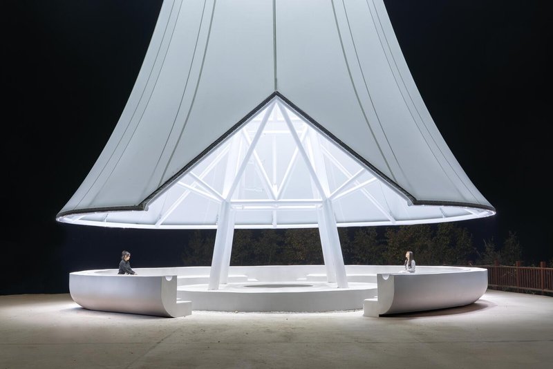 Fire lookout tower at night: illuminated membrane canopy glowing white, steel frame silhouette, curved seating below
