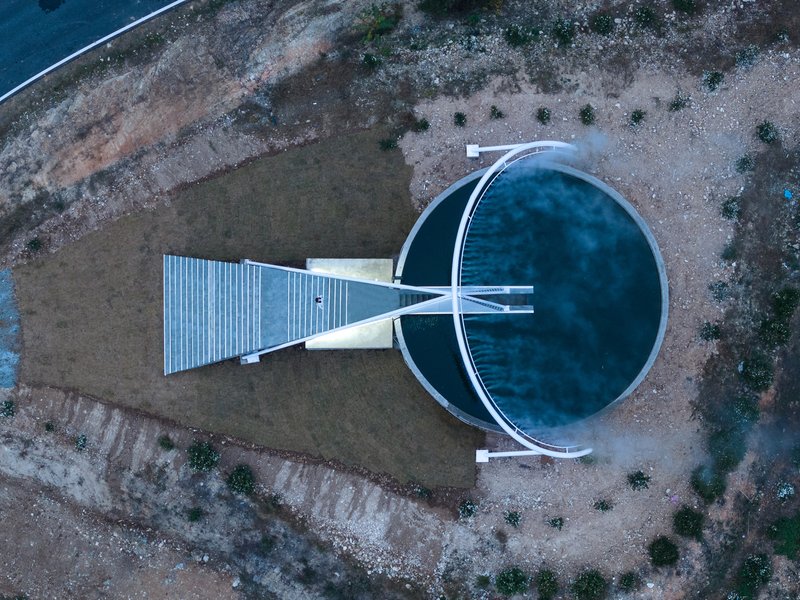 Aerial view of the reservoir intervention: circular water basin, triangular mirrored staircase, and walkway extending to centre