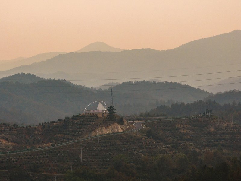 Reservoir from distance: the circular form and arch sitting among tea-oil terraces at golden hour