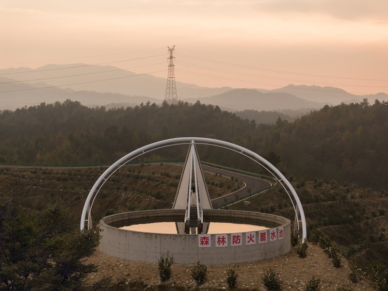 Reservoir at sunset: the steel arch ring, walkway, and circular basin against layered mountains and transmission tower