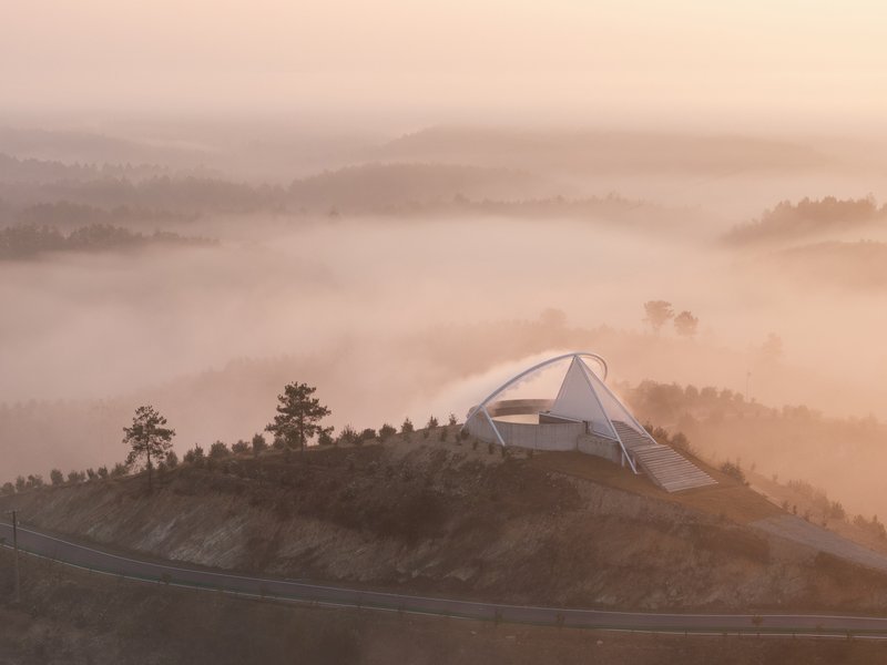 Dawn aerial: the reservoir structure emerging from fog, the walkway and arch catching early light