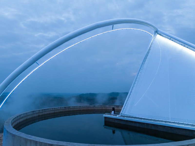 Detail: translucent membrane and steel arch ring over the reservoir water, blue twilight, mist rising