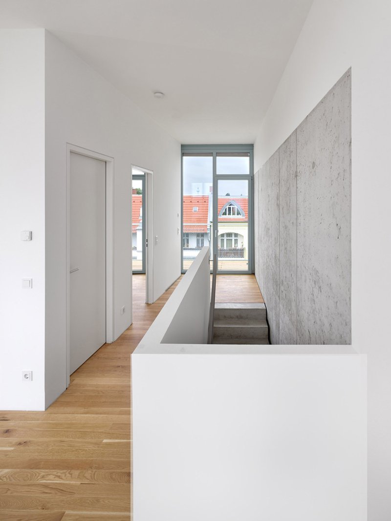 Upper hallway with oak flooring, concrete stairwell wall, and window framing view of neighboring rooftops