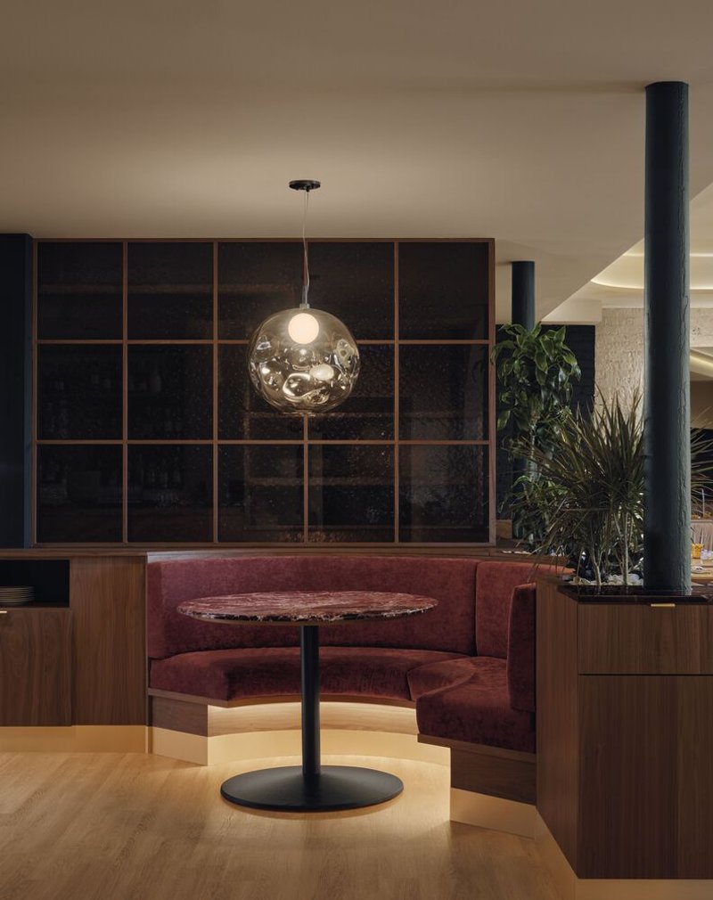 Curved banquette seating niche with spherical glass pendant and dark gridded wall behind potted plants