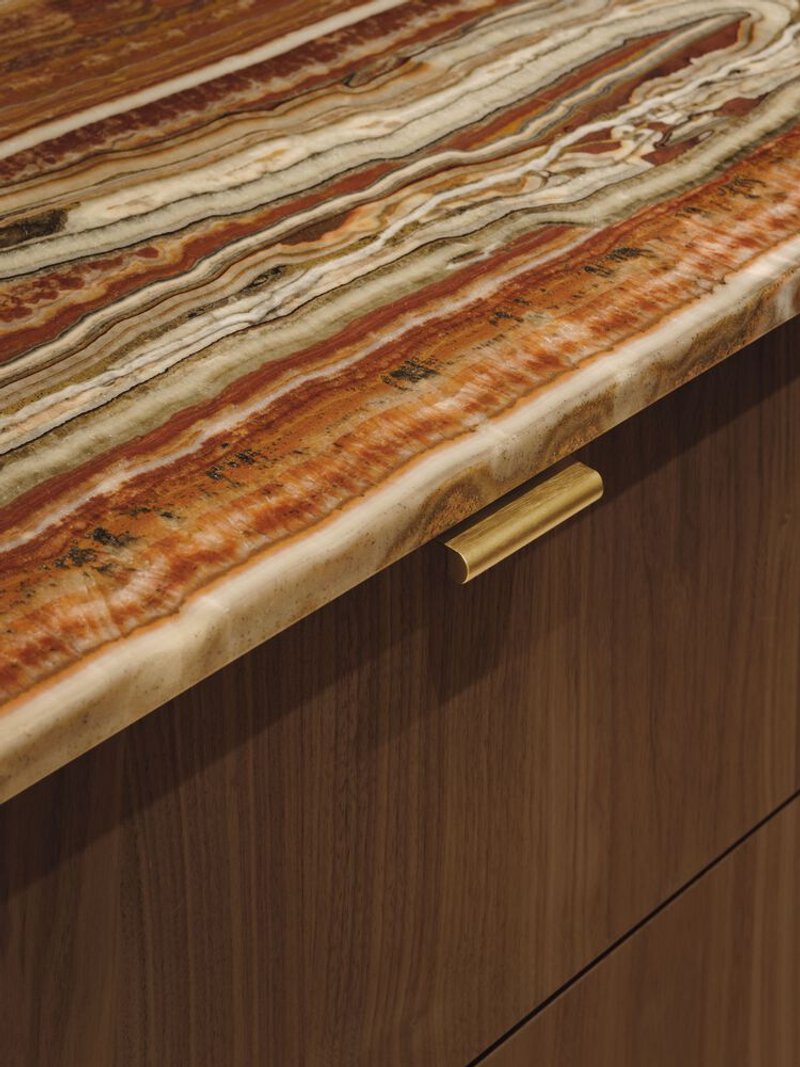 Striated onyx countertop edge with brass drawer pull against timber veneer cabinetry