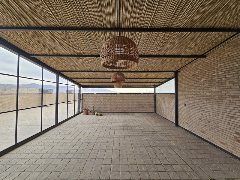 Covered rooftop terrace with woven bamboo ceiling panels and steel-framed glazing overlooking the landscape