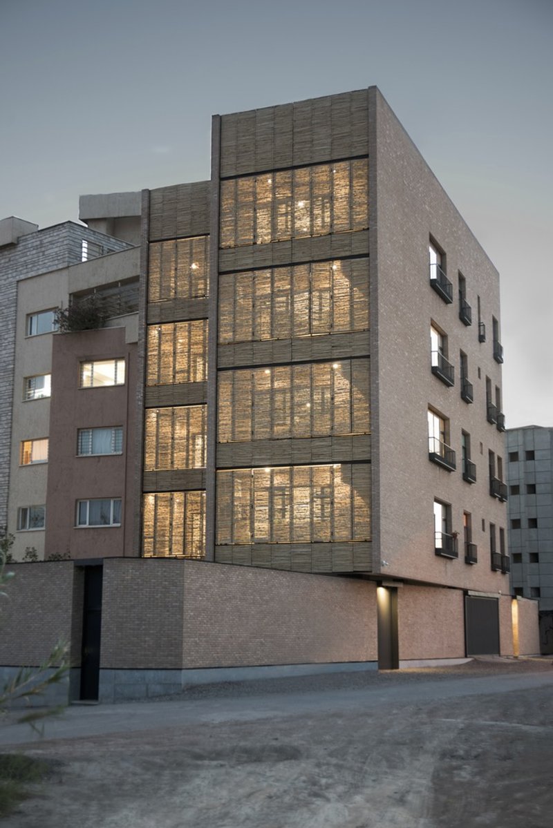 Street facade illuminated at twilight showing vertical bands of woven reed screens behind glass