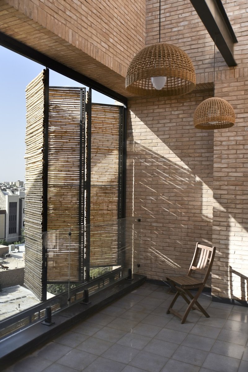 Covered terrace with horizontal reed screen, wicker pendant lights, and folding chair against brick wall